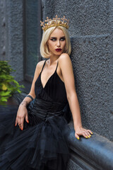 Fashionable woman in black open dress and crown with gothic make up