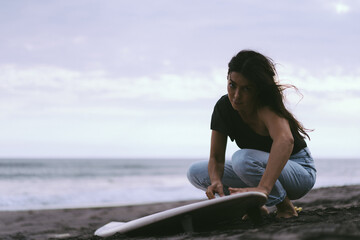 Young woman surfer, preparing a surfboard on the ocean, waxing. Woman with surfboard on the ocean, active lifestyle, water sports.