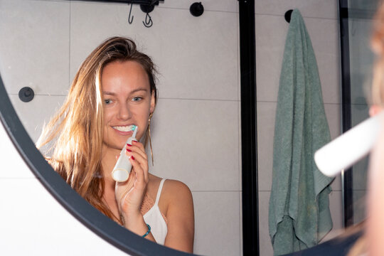 pretty blonde woman brushing her teeth with an electric toothbrush