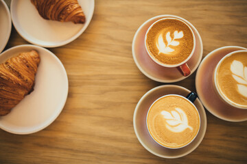 Freshly baked crusty croissants and coffee on wooden table.