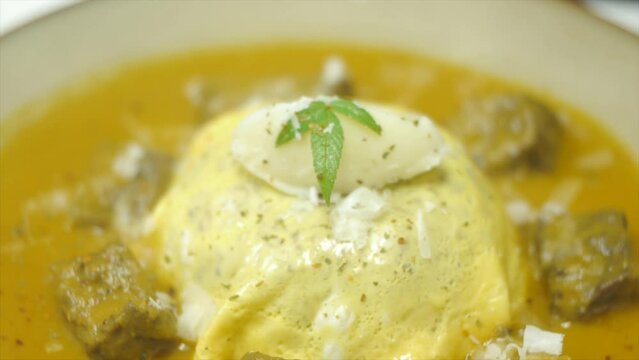 Grated cheese sprinkled over Asian egg and beef curry dish filmed as close up