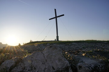 Fototapeta na wymiar Der Sonnenstern am Morgen verleiht dem Gipfelkreuz ein ehrwürdiges Licht.
