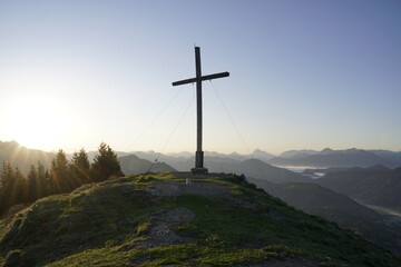 Das mächtige Gipfelkreuz erhebt sich über dem erwachenden Tal.