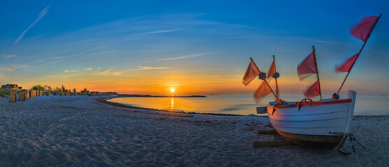 Panorama view of beach on the Baltic Sea at sunset with beach chairs and fishing boat on the sand.