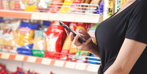 Caucasian woman using smartphone in supermarket.