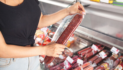 Caucasian woman buying sausage in supermarket.