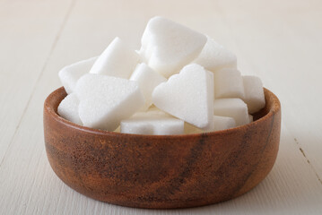 Bridge-shaped sugar cubes in wooden bowl on white wooden background. Low angle closeup view, no people.