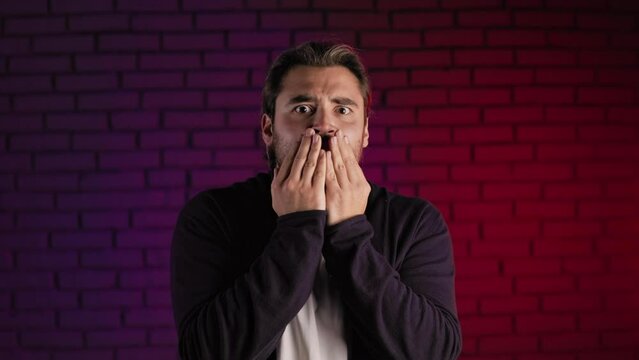 Scared caucasian man looking nervously on camera with open mouth while standing in studio. Human reaction, emotions and fobia.