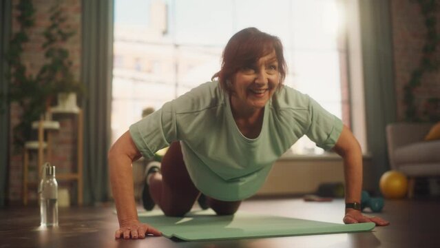 Happy Fit Senior Woman Training on a Yoga Mat, Doing Burpees Exercises During Morning Workout at Home in Sunny Apartment. Healthy Lifestyle, Fitness, Recreation and Retirement.