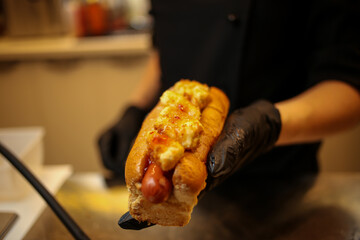 cook in black gloves holds hot dog. The cook prepares a hot dog, adding the sauce to the sausage. hamburgers, hot dog. concept of fast food. cook hot-dog 