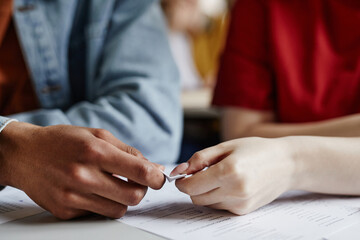 Closeup of two students passing note in secret gossiping or cheating on test, copy space