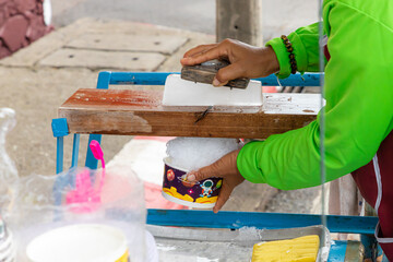 
The seller is scraping ice cubes with a blade on the wood to obtain ice crystals. Used to make desserts, shaved ice Thailand