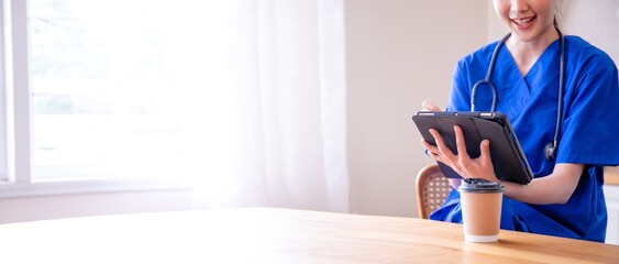 Smiling Asian American female doctor wearing Blue uniform using tablet,standing,browsing medical apps,professional therapist physician working online,chatting,consulting patient,tele medicine,Thai.