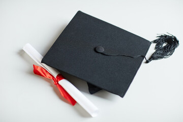 Close up of graduation cap and diploma with red ribbon on white background