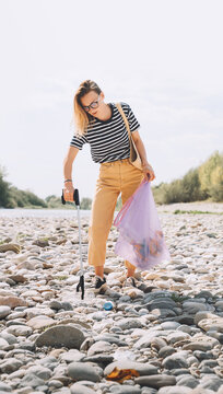 Person help to keep nature clean up and pick up garbage. Young woman clean up outdoor area from rubbish. Volunteer female collecting plastic waste trash on stones of river beach.