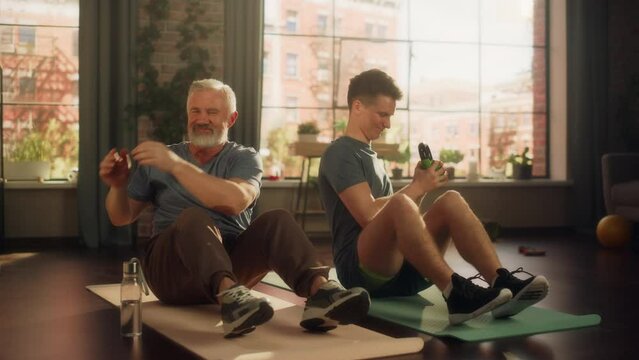 Middle Aged Man Exercising at Home with Personal Trainer. Senior Male Strengthening Core Muscles with Kettlebell Workout. Young Man or Grandchild Supporting and Training with Elderly Man.