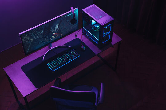 Top view of gamer work space and professional gaming setup: mouse, keyboard, monitor, headset, powerful computer. Premium PC with RGB light inside. Cyber sportsman empty studio with streaming setup