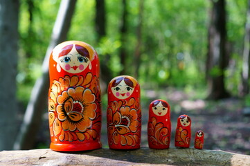 A row of nesting dolls in close-up against a background of green foliage. Slavic culture.