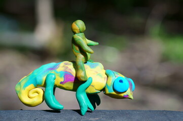 A toy chameleon and a human figure on a colored background.