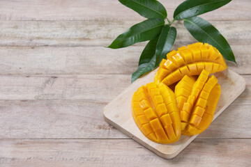 Beautiful chopped ripe mango with green leaves on wooden background, Tropical fruit design concept.