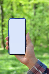Smartphone mockup with white blank screen in the hand. Close up photo outdoors on greenery blurred background. Lifestyle or technology concept