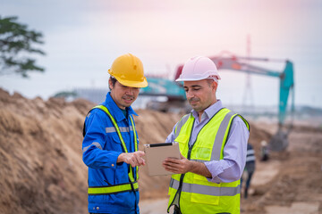 Surveyor engineer wearing safety uniform ,helmet and radio communication with equipment theodolite to measurement positioning on the construction site of the road with construct machinery background