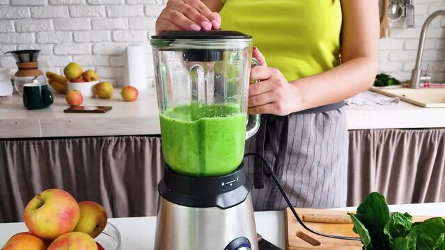 Healthy eating, dieting. front view of woman making green healthy smoothie with blender at the kitchen