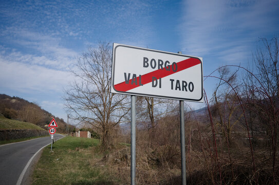 Road Sign End Of Town Borgo Val Di Taro, Parma Province, Italy. Road Sign Indicating Leaving Town With City Name Crossed Out With Red Stripe Against Blue Sky. Speed Limit Of 40 Kmph On Background