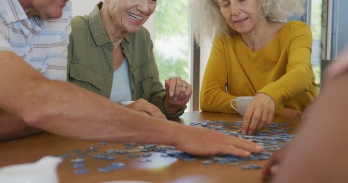 Happy senior diverse people playing puzzle at table at retirement home