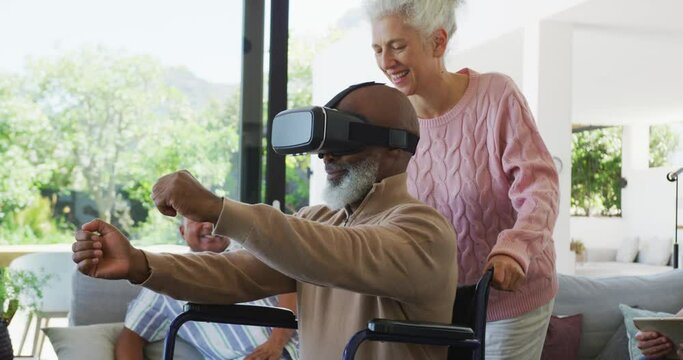 Happy senior diverse people with man in wheelchair using vr headset at retirement home
