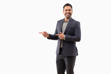 Cheerful young businessman pointing sideways against white background