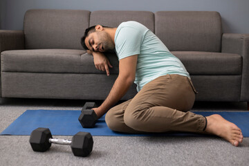 Portrait of tired young man leaning his head on sofa during exercise in living room