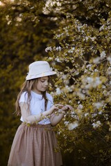 Dziecko w kapeluszu zaciekawione wiosennym, białym drzewem - obrazy, fototapety, plakaty