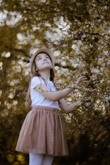 Dziecko w kapeluszu zaciekawione wiosennym, białym drzewem - obrazy, fototapety, plakaty