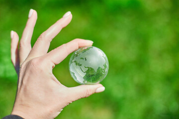 Human hand hold glass Earth globe on green grass background, Saving environment concept.