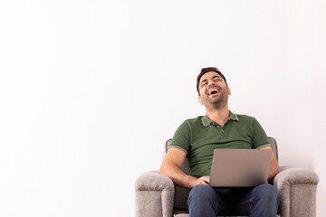 Portrait of happy young man laughing while using laptop on sofa 