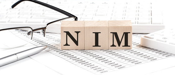 NIM written on wooden cube with keyboard , calculator, chart,glasses.Business concept