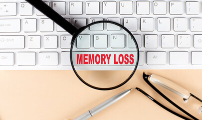 Text MEMORY LOSS on keyboard with magnifier , glasses and pen on beige background