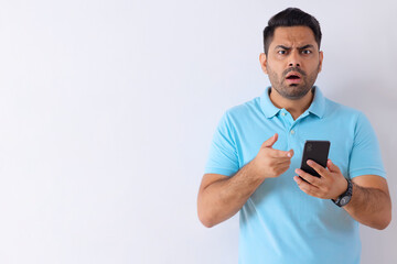 Portrait of a surprised young man standing with Smartphone against white background