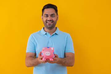 Fototapeta na wymiar Portrait of a cheerful young man holding piggy bank against yellow background