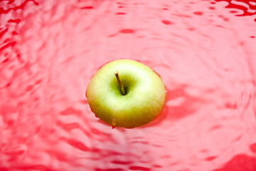 Swimming apple on red background. Water surface with a swimming green apple.