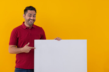 Portrait of a cheerful young man on yellow background pointing at blank placard