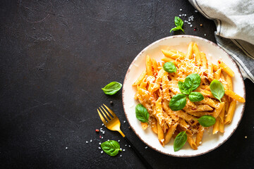 Italian pasta with tomato sauce, basil and parmesan cheese on dark table. Penne pasta with tomato sauce alla arrabbiata. Top view.