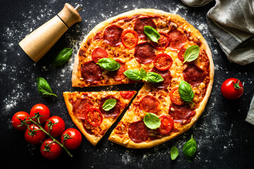 Pizza on black background. Traditional italian pizza with salami cheese, tomatoes and basil. Top...