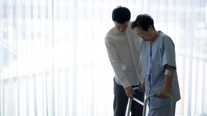 Asian caring loving son helping old injured mother physical theraphy walk with walker hospital