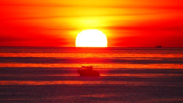 Seascape, sun rising above horizon. Fishing boat on sea water at sunrise orange color light. Nature landscape, early morning.