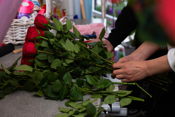 Fototapeta na wymiar Florist at work. Close-up female hands cut roses Woman making a bouquet of red roses for valentines day. Fresh roses for bouquet delivery.