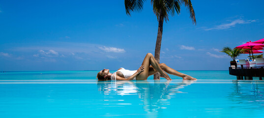 Elegant tanned woman in white swimsuit in pool on tropical Maldives island. Beautiful bikini body...