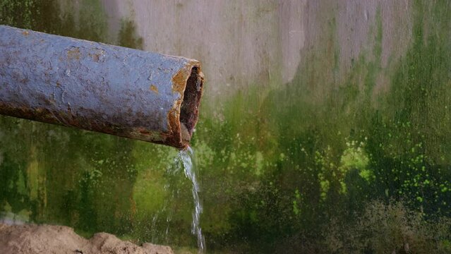 Water flowing from metal drain against wall of old house with stains, mold spots. Stream of rain water gutters down from drainpipe. Drainage of rainwater from roof with building downpipe, downspout