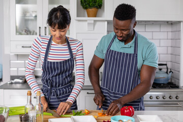 Multiracial young couple chopping vegetables while cooking food together in kitchen at home